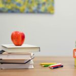 An apple sat on top of a pile of books next to some coloured pencils and 3 blocks spelling out ABC on them vertically