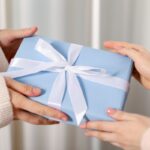 two women exchanging a gift wrapped in blue paper with a white ribbon