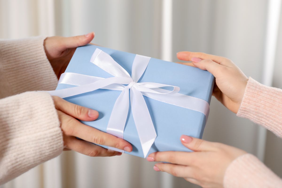 two women exchanging a gift wrapped in blue paper with a white ribbon